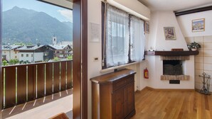 Une pièce avec un plancher en bois, une fenêtre avec des rideaux, une cheminée et une vue sur les montagnes.