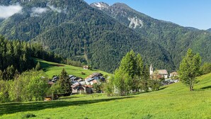 Un village de montagne avec des maisons et une église, entouré d’une végétation luxuriante et sous un ciel dégagé.