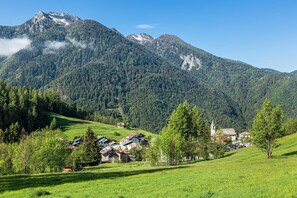 A mountain village with houses and a church, surrounded by lush greenery and clear skies.