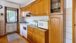 Une cuisine avec des meubles en bois, un four à micro-ondes, une cuisinière et une fenêtre avec des rideaux.