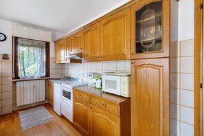 A kitchen with wooden cabinets, a microwave, a stove, and a window with curtains.