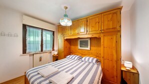 Une chambre à coucher comprenant un lit, une armoire en bois, une fenêtre avec des rideaux et un luminaire suspendu.