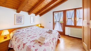 Un dormitorio con techo de madera, una cama con edredón estampado, dos lámparas de noche y una ventana con cortinas.