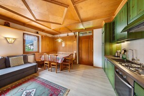 Une pièce chaleureuse avec un canapé, une table à manger et des chaises, un plafond en bois et des armoires vertes.