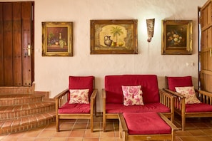 Ein Zimmer mit Holztür, einer Treppe, einer Sofagarnitur mit blumigen Kissen und drei gerahmten Kunstwerken an der Wand.