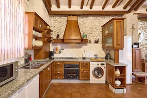 Una cocina con encimeras de granito, armarios de madera, salpicadero de piedra, horno empotrado, lavadora y microondas.