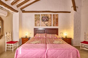 Ein Schlafzimmer mit Holzbalkendecke, einem Bett mit rosa Bettwäsche, zwei Nachttischen mit Lampen sowie einem an der Wand hängenden Gemälde.