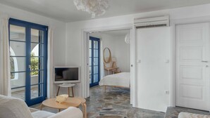 A room with a stone floor, a bed, a TV, a sofa, and a dining table. - Country house "Agios Sostis" with a jacuzzi and close to the beach (Serifos)