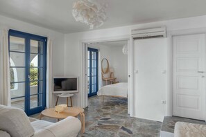 A room with a stone floor, a bed, a TV, a sofa, and a dining table. - Country house "Agios Sostis" with a jacuzzi and close to the beach (Serifos)