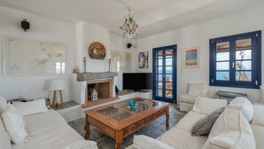 A living room with a fireplace, a television, and a large window with a view. - Country house "Agios Sostis" with a jacuzzi and close to the beach (Serifos)