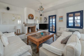 A living room with a fireplace, a television, and a large window with a view. - Country house "Agios Sostis" with a jacuzzi and close to the beach (Serifos)