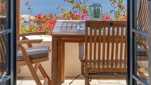 An open patio with a wooden table and chairs, a glass table lamp, and a view of the sea and a distant island. - Country house "Agios Sostis" with a jacuzzi and close to the beach (Serifos)