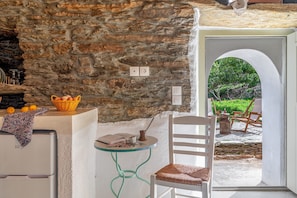 Un muro de piedra, una silla blanca, una mesa con una cesta, y vistas a la vegetación.