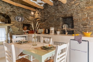 Una cocina rústica con paredes de piedra, una mesa de comedor con sillas, un refrigerador y varios electrodomésticos.