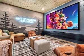 Un salon moderne doté d’un grand téléviseur à écran plat, de sièges confortables et d’un mur décoratif sur le thème de la montagne.