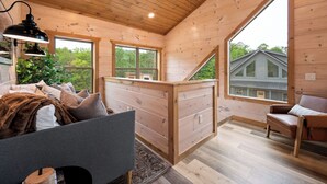 A cozy cabin interior with a bed, a desk, and a large window offering a view of a house and trees. - Central Loc*Luxury*Indoor Pool *Hot Tub *Dollywood (Pigeon Forge)