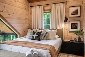 Camera da letto con pannelli in legno, un letto, tende, quadri appesi e un comodino.