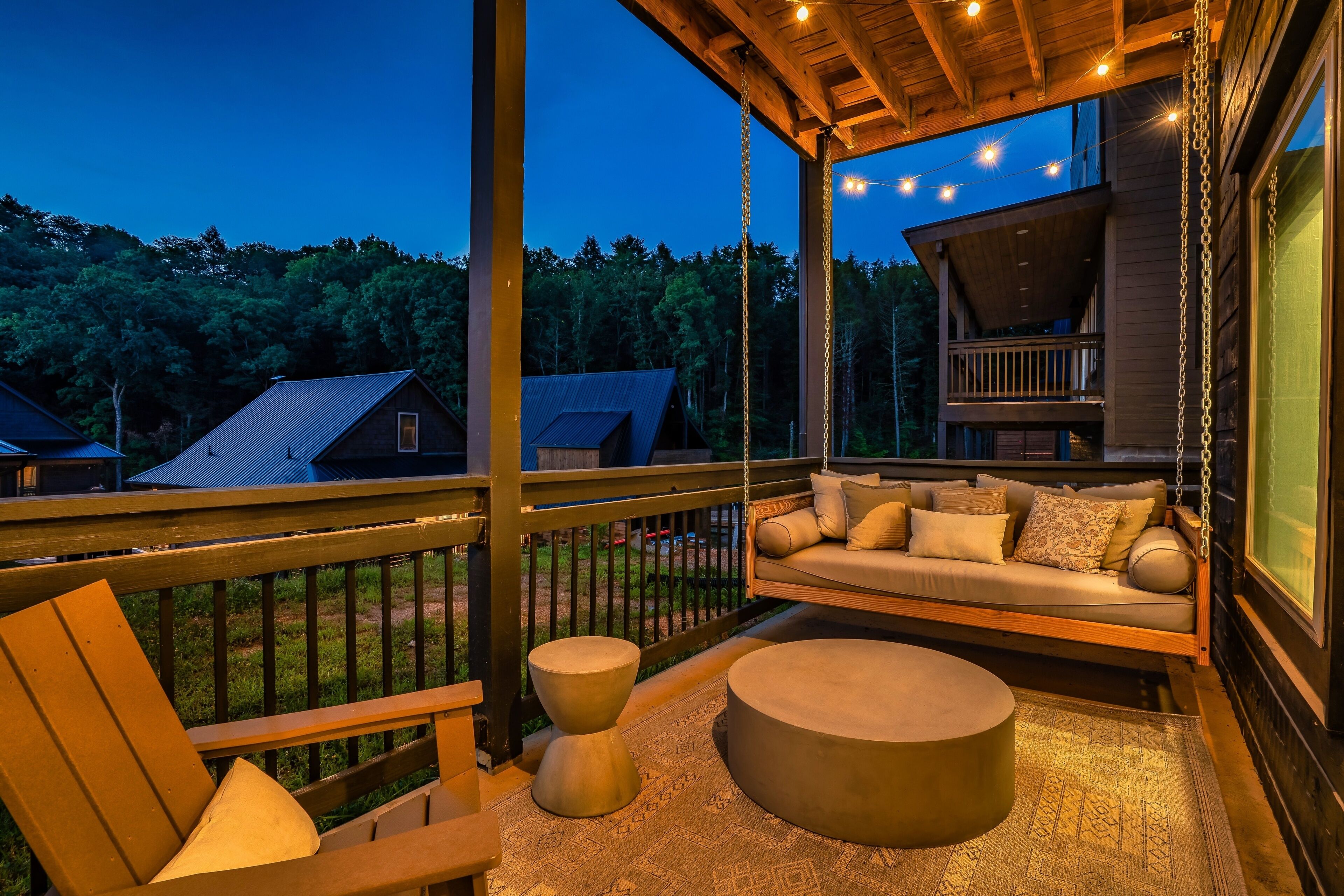 A wooden deck with a hanging chair, a sofa, and a round ottoman.