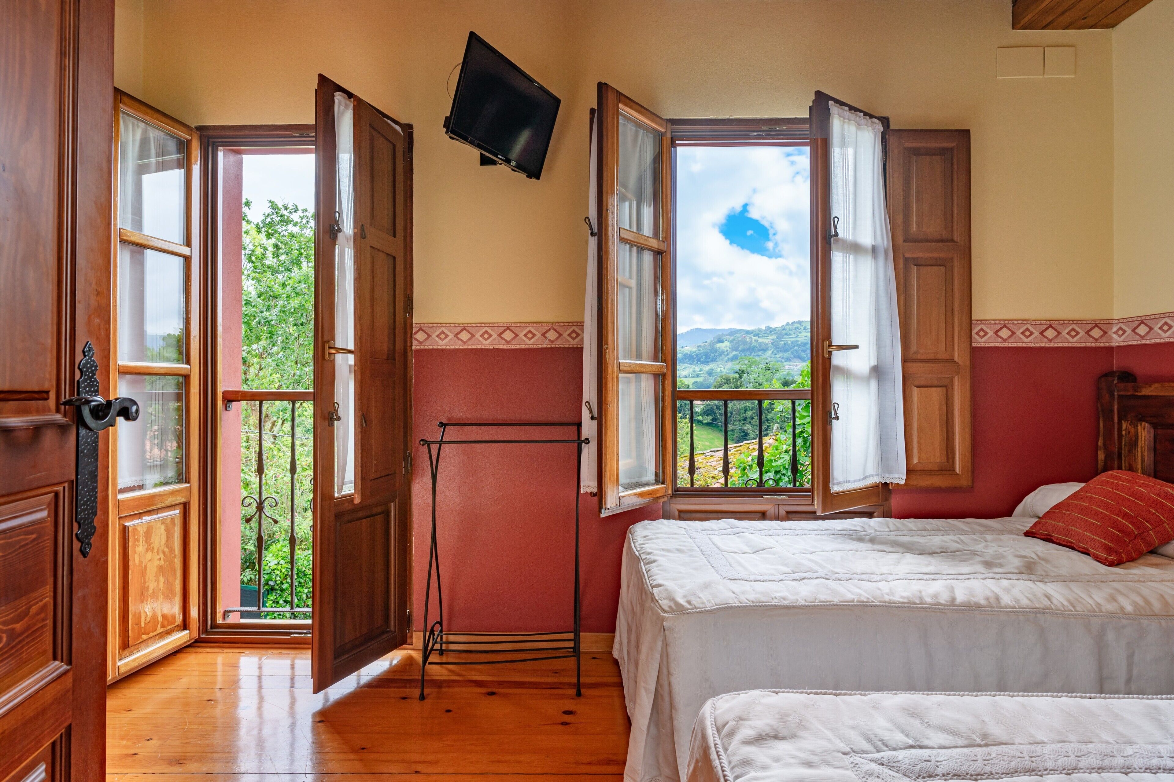 A bedroom with a bed, a TV mounted on the wall, and a balcony with open doors.