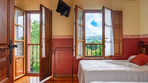 Un dormitorio con cama, televisor montado en la pared y balcón con puertas abiertas.