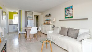 Ett modernt vardagsrum med en vit soffa, ett glasbord och en matplats med vita stolar.