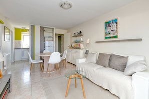 Un salon moderne avec un canapé blanc, une table basse en verre et un coin repas avec des chaises blanches.