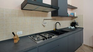 A kitchen with a gas stove, a sink, a knife block, and a coffee maker. - Villa 'Il Frutteto 49' with Private Terrace and Wi-Fi (Ortovero)