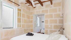 Une chambre à coucher avec un lit, une fenêtre, une porte et un mur en pierre.