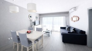 Una sala de estar moderna con comedor, un sofá negro y un televisor.