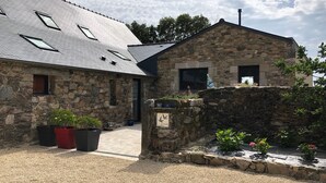 Un bâtiment en pierre avec un toit en pente, une allée gravillonnée et un mur en pierre sur lequel est apposée une enseigne.