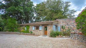 A stone house with a gravel driveway, wooden shutters, and a door.