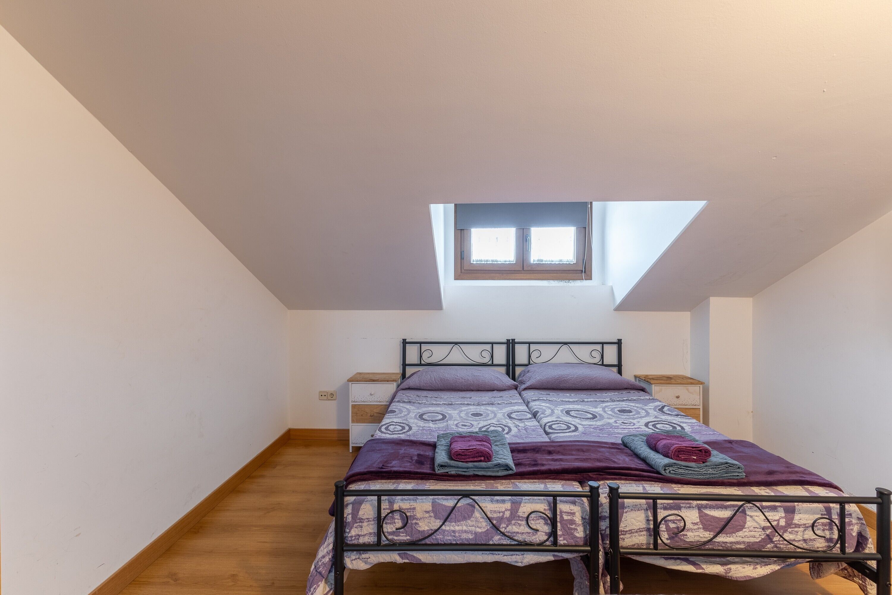 Une chambre avec un plafond en pente, un puits de lumière, un lit avec une literie à motifs et une table de chevet.