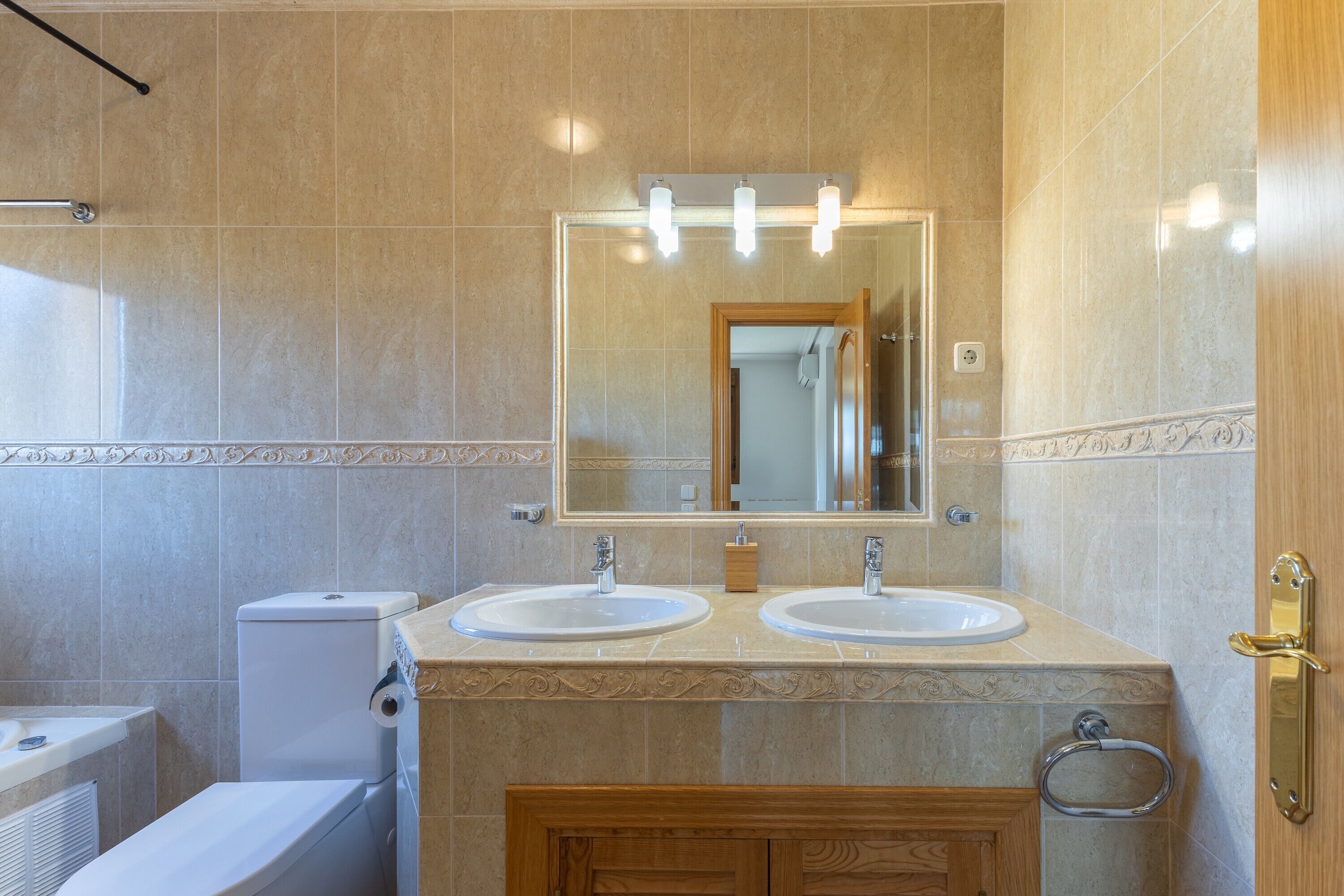 Un baño con dos lavamanos, un inodoro, un espejo con iluminación y un perchero para toallas.