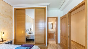 Una camera da letto con un letto, un comodino, una lampada, un armadio in legno e un bagno visibile nello specchio.