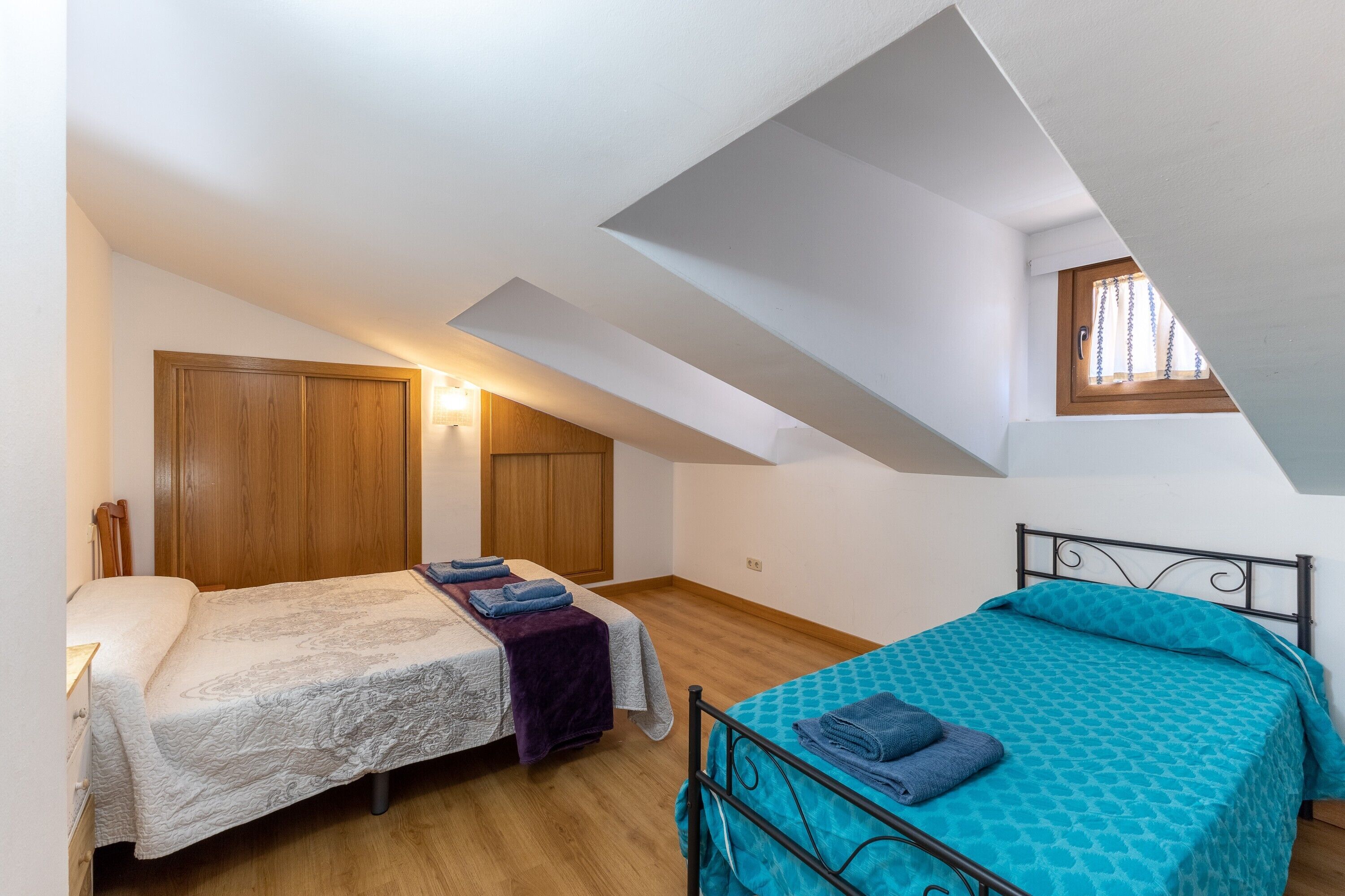 Un dormitorio con dos camas, armarios de madera, un ventanal y techo inclinado.