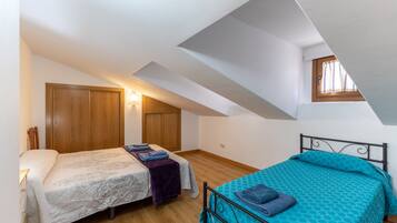 Un dormitorio con dos camas, armarios de madera, un ventanal y techo inclinado.