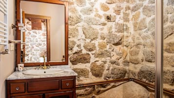 Een badkamer met een stenen muur, een houten wastafelmeubel, een wastafel en een spiegel.