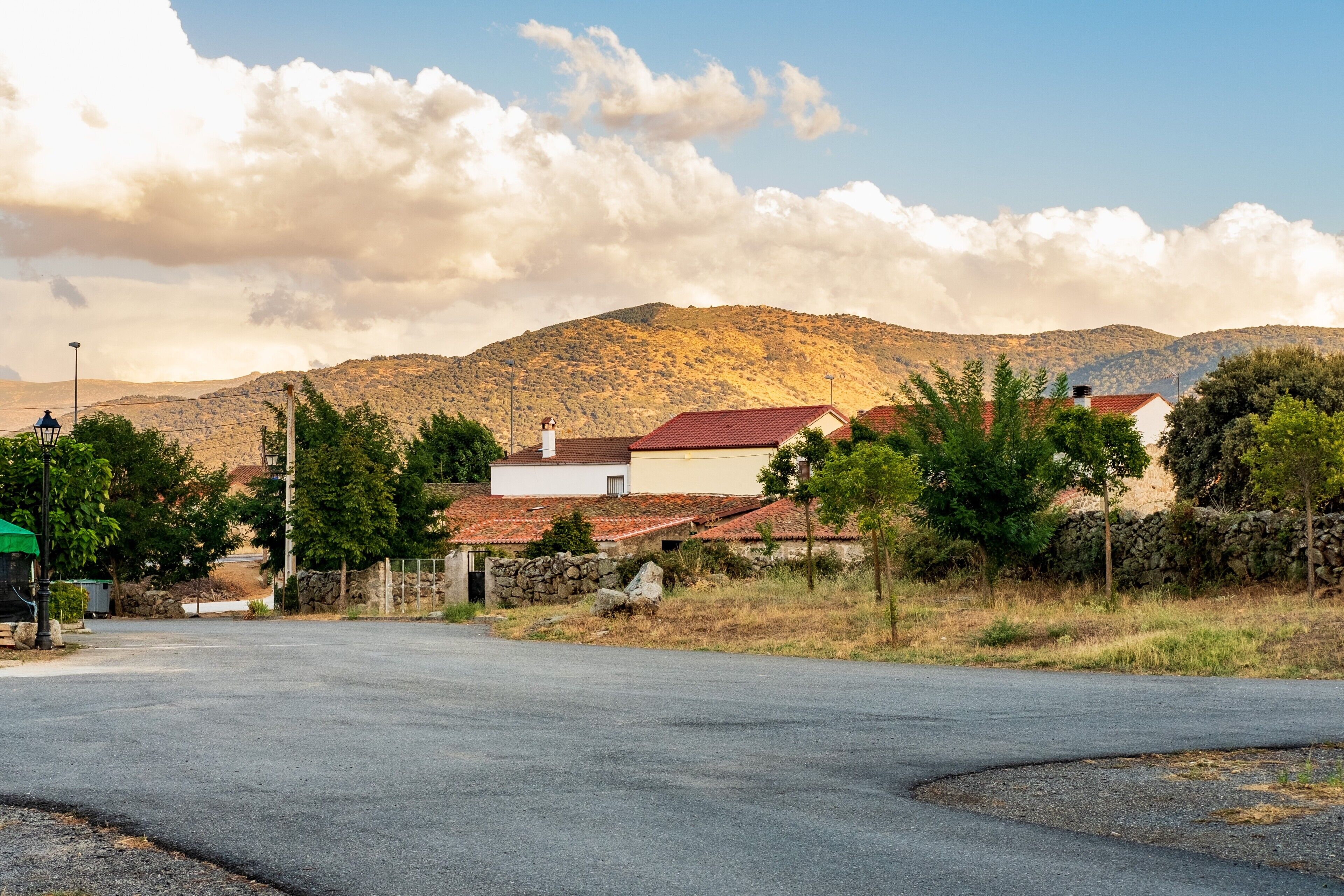A rural road with houses, a stone wall, and a mountain in the background.