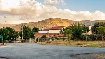 A rural road with houses, a stone wall, and a mountain in the background.