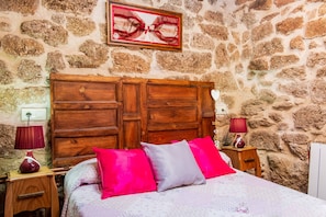 A bedroom with a stone wall, wooden headboard, two bedside tables with lamps, and a bed with patterned bedding and pillows.