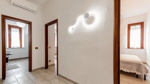 Ein Zimmer mit einem Bett, einer Wandleuchte und einer Tür zu einem weiteren Raum.