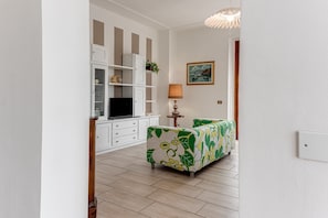 A room with a TV, white cabinets, a green sofa, a lamp, and a painting on the wall.