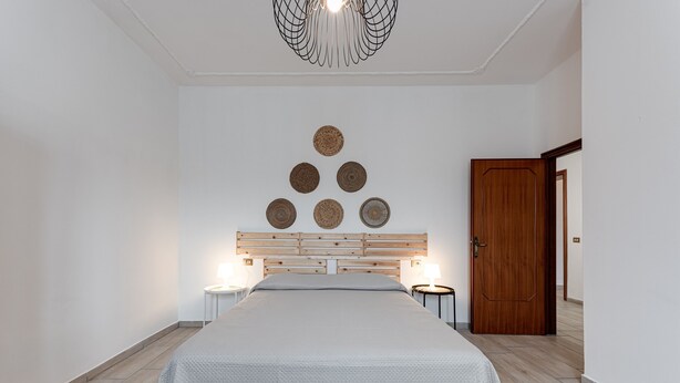 Ein Schlafzimmer mit einem Bett, einem Holz-Kopfteil, einer Wanddekoration in Kreisform, einer Tür und einem Nachttisch mit Lampe.