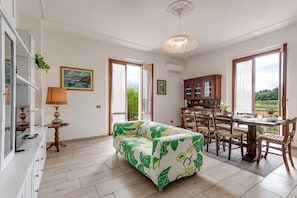 A spacious living area with a sofa, dining table, chairs, and a view through the open door.