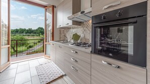 Eine moderne Küche mit einem großen Backofen, einem Gasherd und Blick auf eine grüne Landschaft durch eine Glastür.
