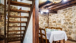 Ein Essbereich mit Steinwand, Holztisch, Stühlen und einer Treppe.