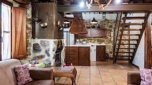 Ein rustikaler Innenraum mit Steinwand, Holzmöbeln, Kamin und Küchenbereich.