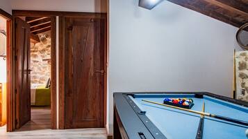 Una mesa de billar con taco, una puerta de madera y una pared de piedra.