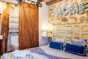 A bedroom with a wooden wardrobe, a bed with patterned bedding, a stone wall with 'HOME' decor, and a white radiator. - Holiday Home 'La Cantina' with Mountain Views (Villar de Corneja)