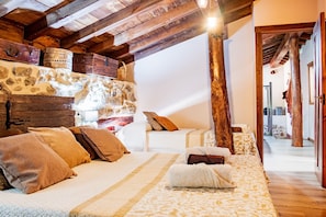 Quarto rústico com parede de pedra, vigas de madeira e cama com roupa de cama estampada.